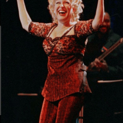 Female singer in a red sequined outfit performing on stage with arms raised.
