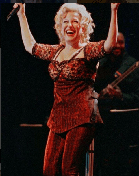 Female singer in a red sequined outfit performing on stage with arms raised.