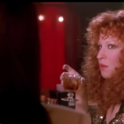 Red-haired woman in a sequined dress holding a cocktail glass at a dimly lit bar.