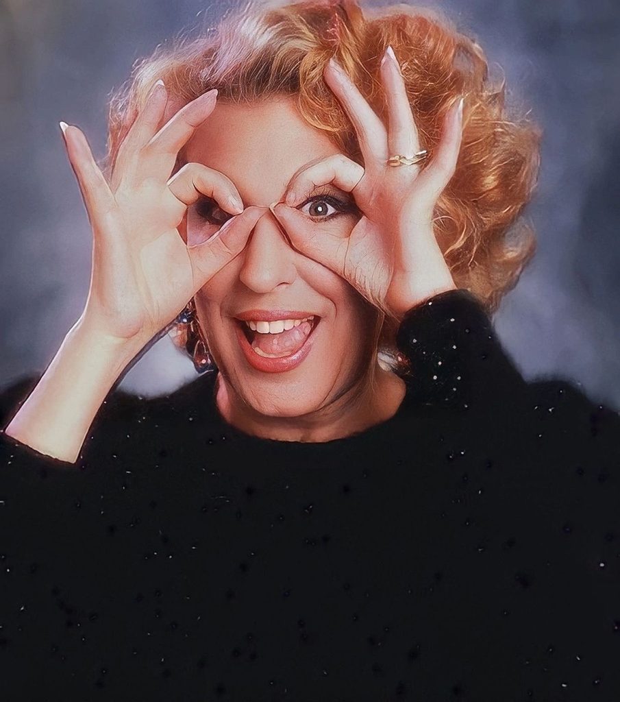 Smiling woman with curly blonde hair making binocular-like circles with her fingers over her eyes.