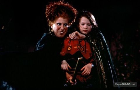 A scary scene where an older, wild-haired woman in a dark cloak confronts a frightened girl in a red outfit in a dark, tense setting.
