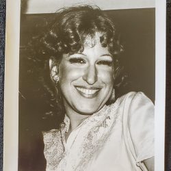 Black-and-white portrait of a smiling woman with curly hair, wearing a lace blouse and earrings.