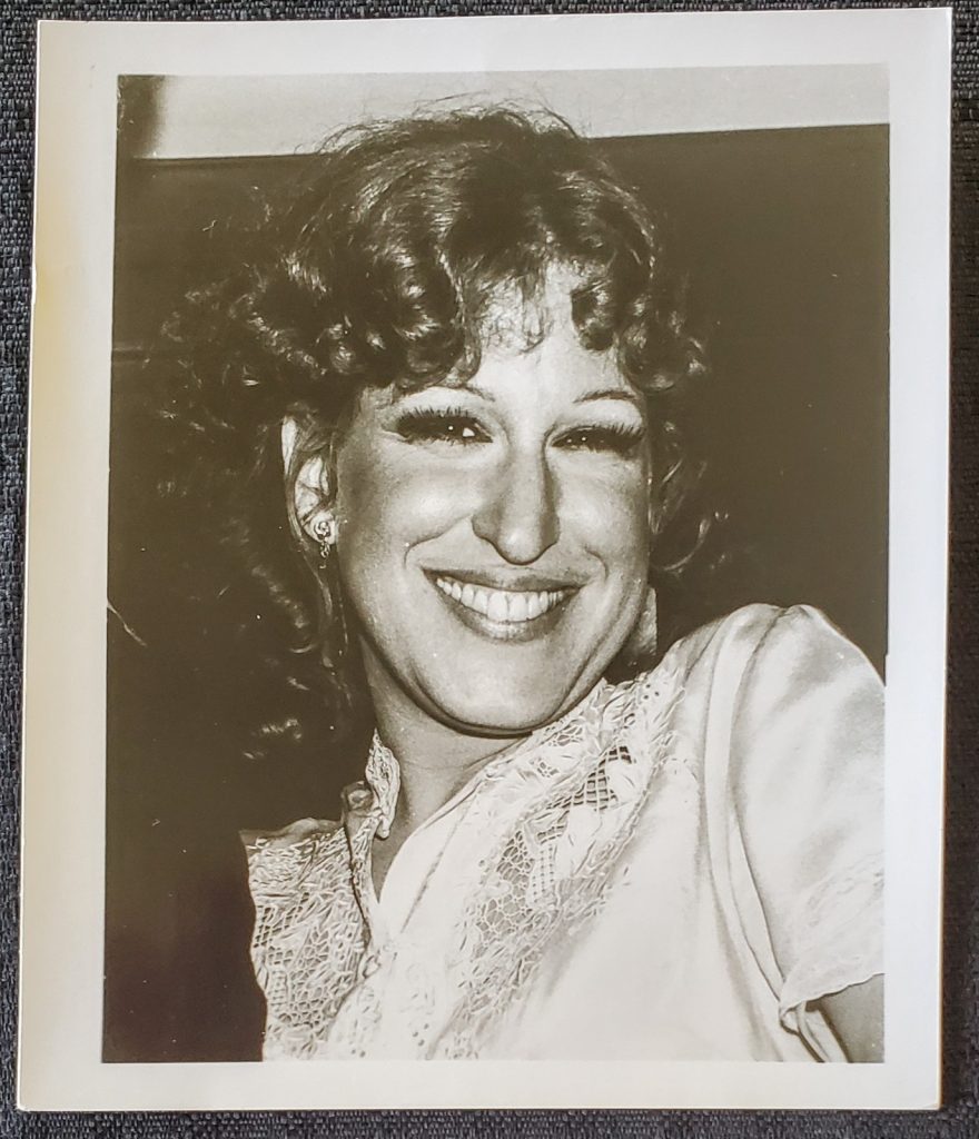 Black-and-white portrait of a smiling woman with curly hair, wearing a lace blouse and earrings.
