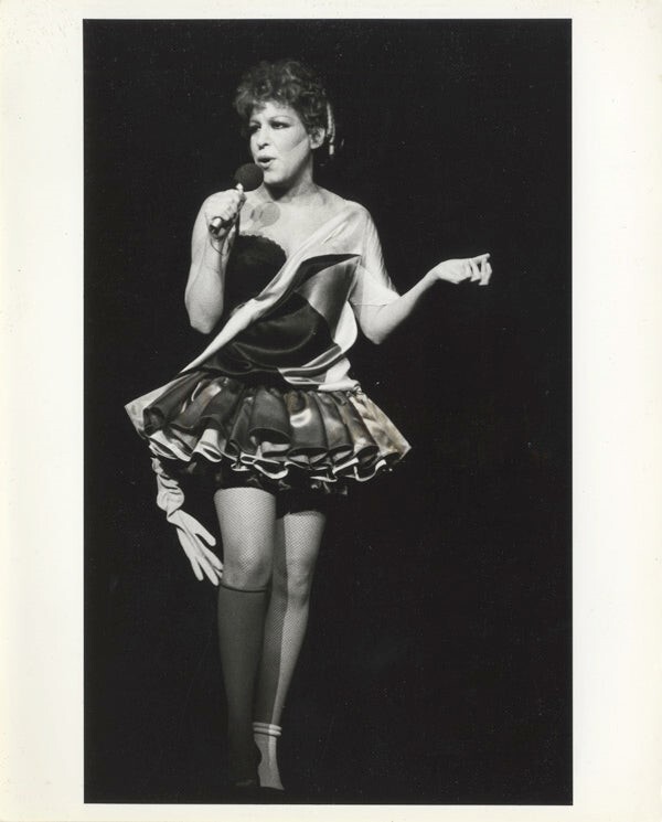 Female singer performing on stage in a short, ruffled satin dress, holding a microphone.