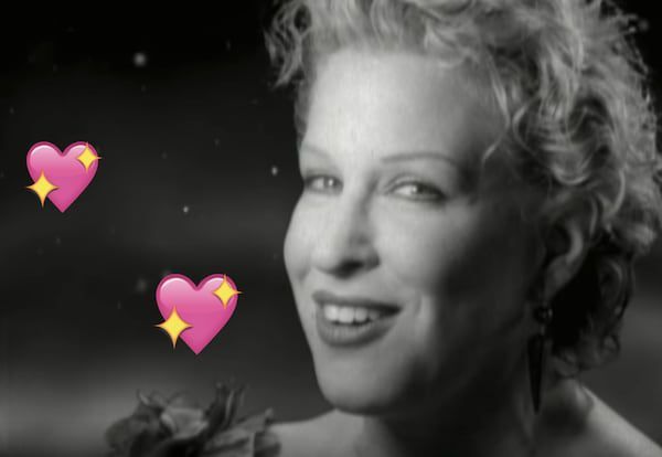 Black-and-white portrait of a smiling Bette Midler with short curly hair, surrounded by two pink heart emojis.