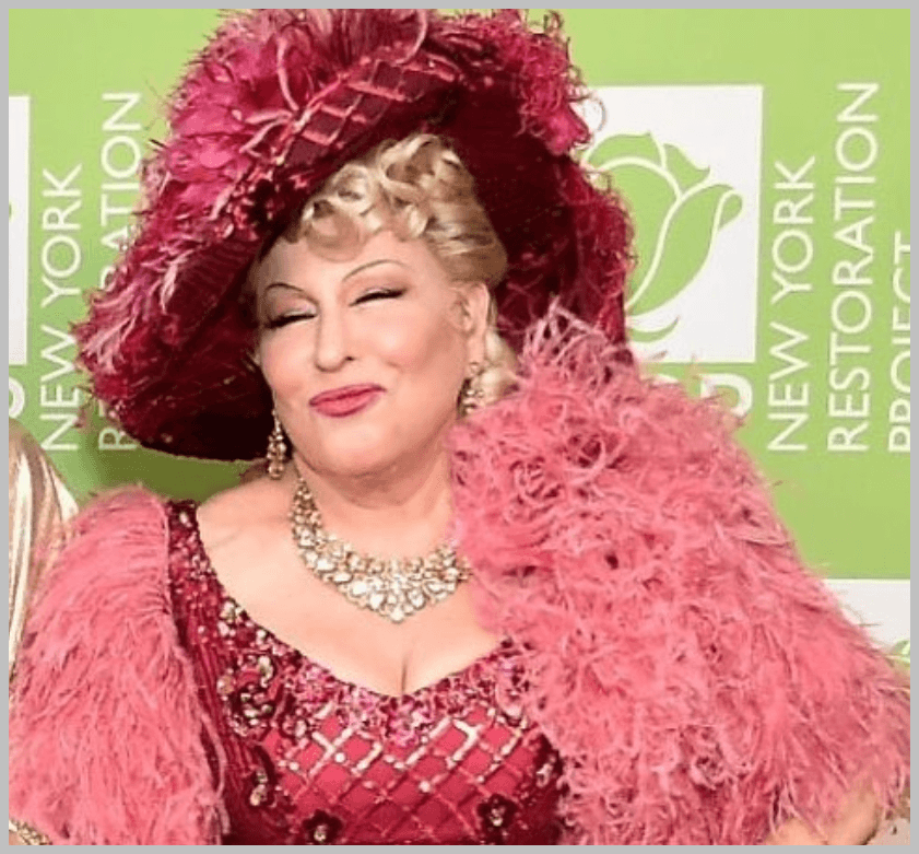 Bette Midler wearing a bright pink sequined gown with a large feather hat, posing and smiling at a New York Restoration Project event.