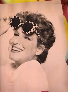 Vintage photo of a smiling woman with black-and-white checkered sunglasses and a retro hairstyle, looking over her shoulder.