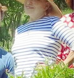 Woman wearing a wide-brimmed straw hat and blue-and-white striped shirt, smiling outdoors among greenery.