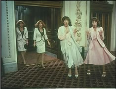 716333a06183bd98d11f518aee03caeb - bootleg betty Four women in mod 1960s dresses walking down a carpeted, ornate hallway in a mansion, posing as if arriving for a scene.