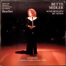 Album cover for Bette Midler's 'Wind Beneath My Wings' showing Midler standing on a lit stage in a black dress, singing into a microphone.