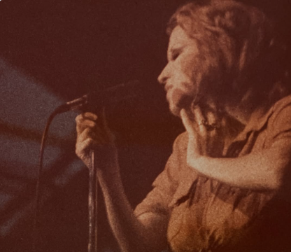 Performer singing into a microphone on stage in a sepia-toned image.