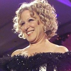 497383744_1142210331283366_5413575195435375298_n - bootleg betty Woman smiling on stage wearing a black-and-white striped off-shoulder gown with feather detail at the neckline.