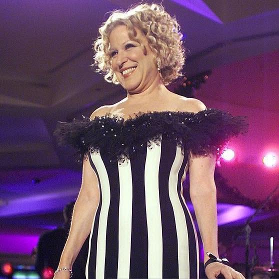 497383744_1142210331283366_5413575195435375298_n - bootleg betty Woman smiling on stage wearing a black-and-white striped off-shoulder gown with feather detail at the neckline.