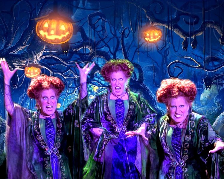 4fad854def923fd42976d3241985c08c - bootleg betty Three witches with bright red curls in green cloaks perform on a dark, forest-themed stage, arms raised and snarling under neon Halloween lighting.
