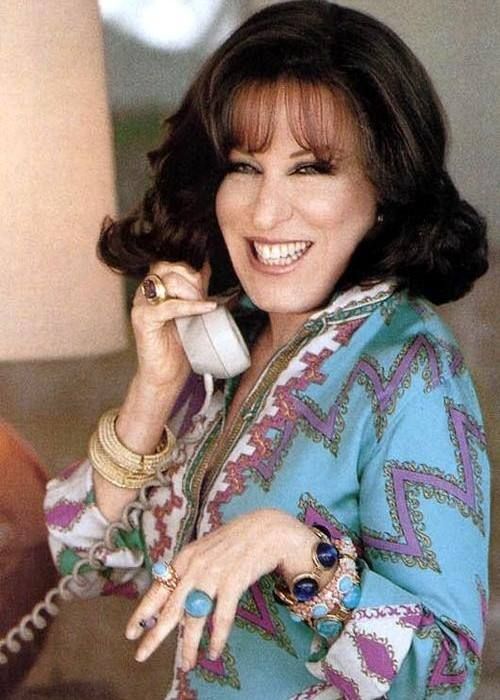 6b5652fd896827f8ff9193c95d9da647 - bootleg betty Smiling woman on a landline phone wearing a turquoise patterned blouse and gold jewelry lined with rings and bracelets.