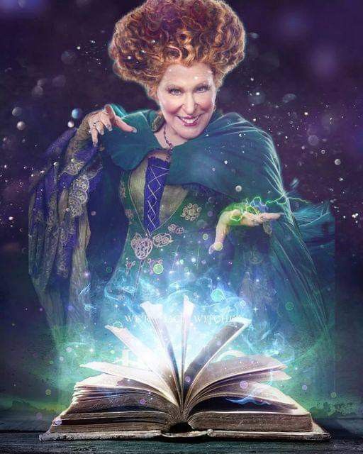 A woman in a green cloak casts a spell from an open glowing book, sparks rising from its pages in a magical scene.