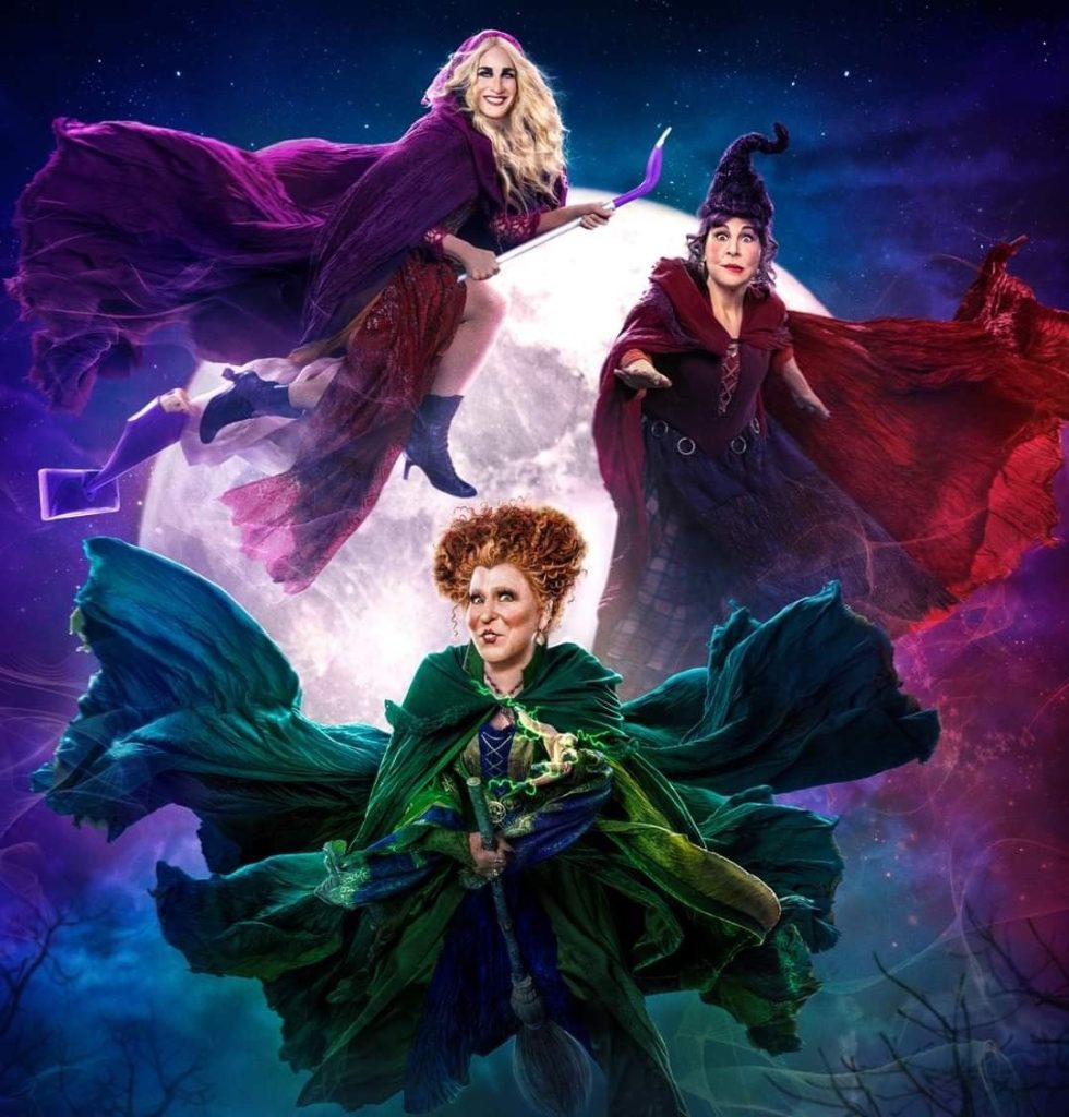 D23f651ddbc928c03425336ff0c88b17 - bootleg betty Three witches in colorful capes flying on broomsticks against a full moon and night sky, a fantasy-themed poster image.