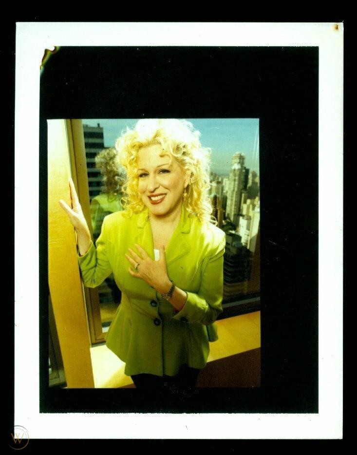 Smiling blonde woman in a lime green blazer stands by a window with a city skyline behind her, posing for a photo.