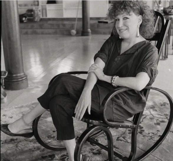 Smiling woman with curly hair sits in a chair in a spacious indoor area.