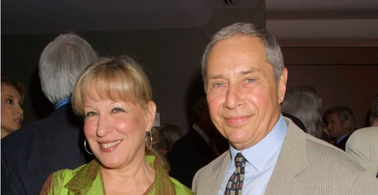 Two smiling adults posing at a social event, with a woman in a lime green jacket on the left and a man in a beige suit on the right.