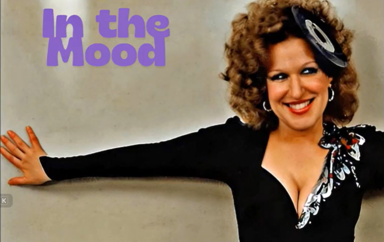 2026-08-19_05-02-58 - bootleg betty Album cover: smiling woman in a black outfit with outstretched arm, beige background, purple 'In the Mood' text in the upper left.