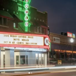 Night view of Cain's Ballroom with a glowing marquee advertising the 2026 Woody Guthrie Prize — Bettie Miller, Oct 16 at Cain's Ballroom on a neon-lit street night scene.