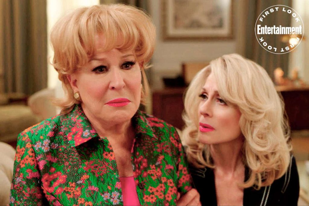 Two blonde women indoors; one in a bright floral jacket looks ahead, the other leans in with a concerned expression; Entertainment Weekly watermark in corner.