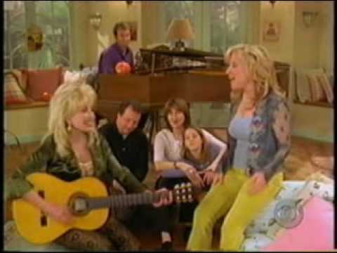 Five people in a cozy living room; a woman plays a yellow guitar while others smile and watch.