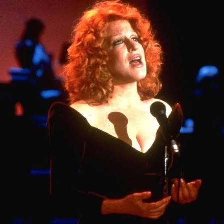Woman with curly red hair singing into two microphones on a dark stage.