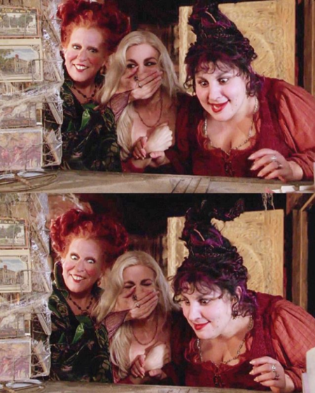 Three women in Halloween costumes peek from behind a wooden shelf, one covering her mouth in surprise, all smiling playfully.