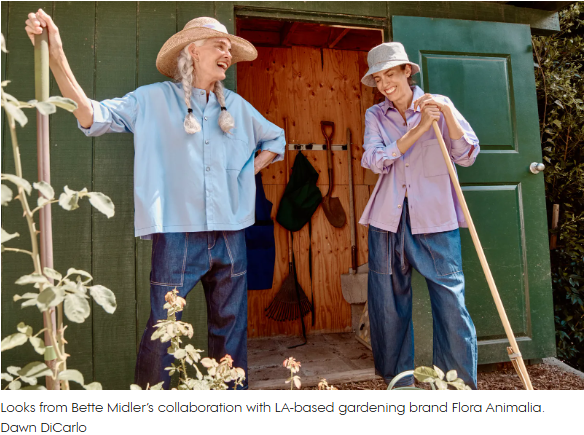 Two elderly women in wide-brimmed hats stand outside a garden shed, smiling; one leans on a rake, the other on a garden hoe with tools visible inside.