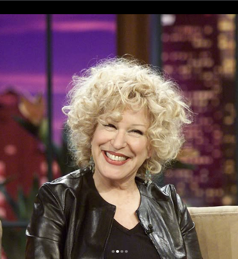 2026-09-05_10-41-43 - bootleg betty Smiling woman with curly blonde hair wearing a black leather jacket during a talk-show interview set.