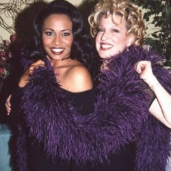Two smiling women posing together in purple feather boas at a party or event.