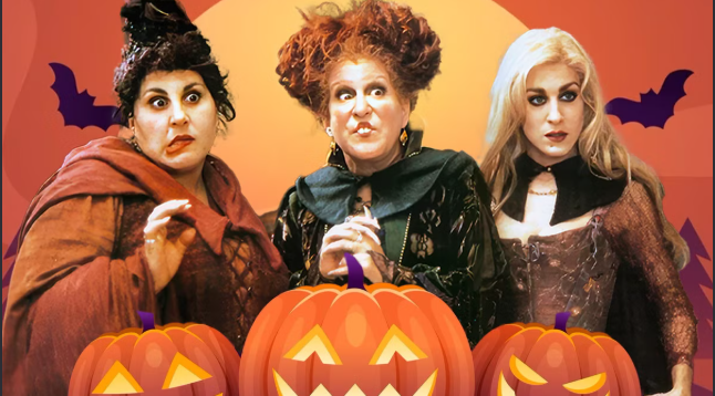 Three women dressed as witches posing behind a row of carved jack-o'-lanterns in a Halloween scene.