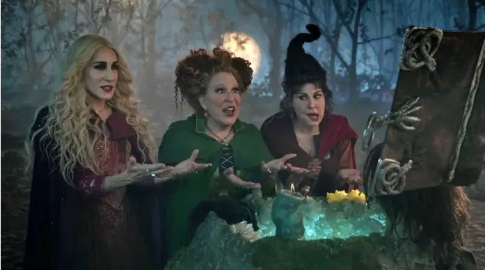 Three witches stand around a glowing cauldron in a moonlit forest, gesturing as they cast a spell.