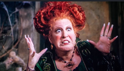 Woman with bright red, curly hair in a green velvet dress, reaching up with startled, wide-eyed expression in a dramatic pose.