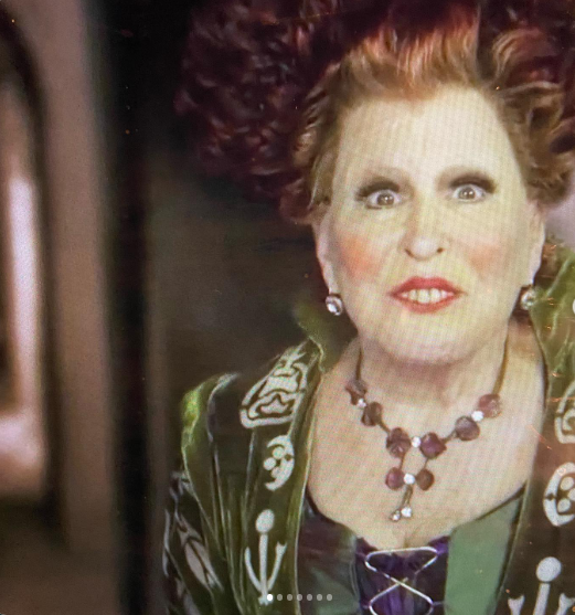 Portrait of a surprised woman with red hair, wearing a green jacket and beaded necklace.