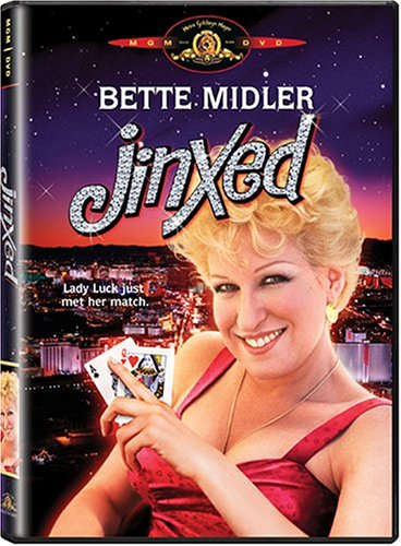 Version 100 - bootleg betty DVD cover for the film Jinxed, featuring a smiling blonde woman in a red dress holding playing cards against a cityscape at dusk.